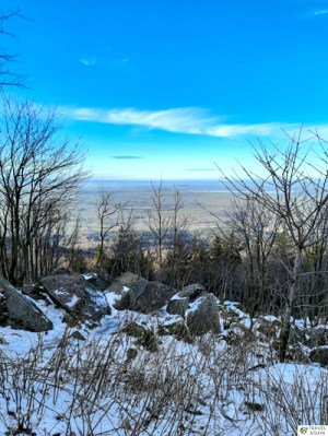 Widok ze szczytu Ślęży na Zalew Mietkowski. Na górze śnieg, na dole zieleń.